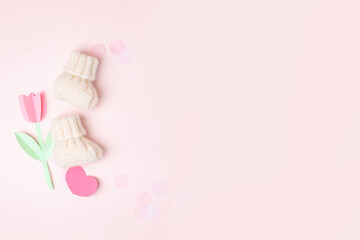 Pair of small white baby socks with and paper decorative flowers on pink background with copy space...