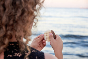 A woman gently holds a seashell in her hands at the sea.