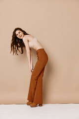 Naklejka premium woman in trousers and a shirt bent over to the side on a beige background in full growth