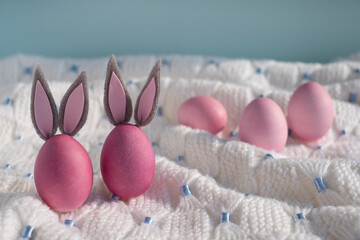 Two pink easter eggs with bunny ears close up on a white knitted blanket