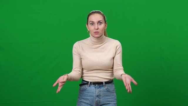 Shocked young woman excusing herself at chromakey background. Middle shot portrait of slim beautiful Caucasian lady making excuse defending on green screen.