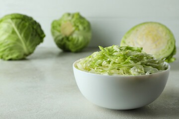 Bowl with sliced cabbage and fresh cabbage on white textured table