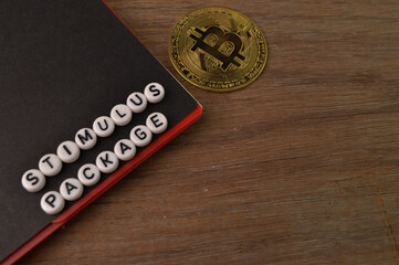 Top angle view of notebook, golden bitcoin and alphabet beads with text STIMULUS PACKAGE.