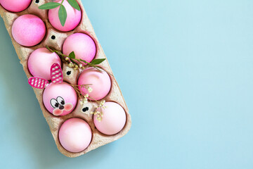 Minimal Easter concept. Festive spring mood, paper box with Easter eggs in pink tones and gerbera flower on pastel blue background. Top view flat lay. Copy space.