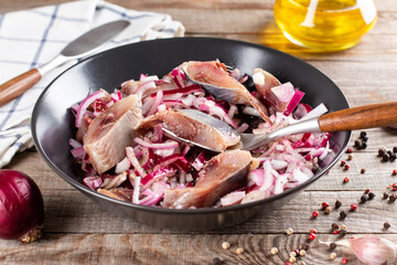 Herring with red onions in black bowl on a wooden table