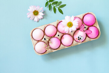 Minimal Easter concept. Festive spring mood, paper box with Easter eggs in pink tones and gerbera flower on pastel blue background. Top view flat lay.