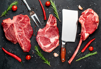 Three raw beef steaks for grilling - rib-eye steak, T-Bone steak, Tomahawk steak on stone background