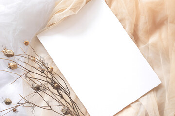 flat lay with white blank paper sheet and dry flowers on beige and white tulle fabric