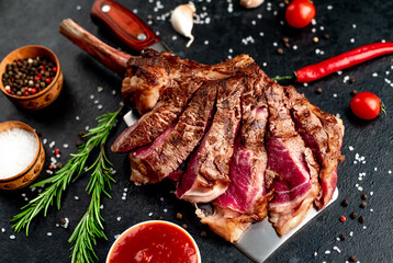Tomahawk beef steak with spices on a knife on a stone background