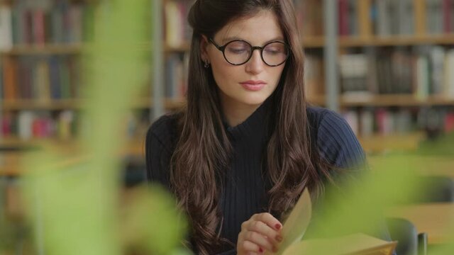 young, beautiful woman is reading a book in a library. Student and learning concept.