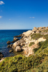 Fototapeta na wymiar Small cliffs and a rocky shore at Prajjet Bay or Anchor Bay at Popeye Village in Malta.