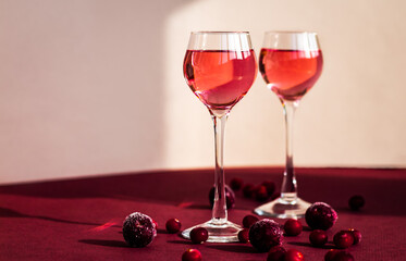 two glasses with pink gin infused with cranberry, light and shadow on the background, berry liqueur or red alcoholic cocktail, copy space, minimalism