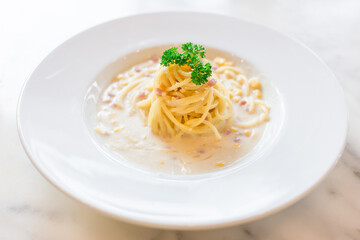 Spaghetti in white cream sauce mixed with ham and corn and served on a white plate in Italian food restaurant.
