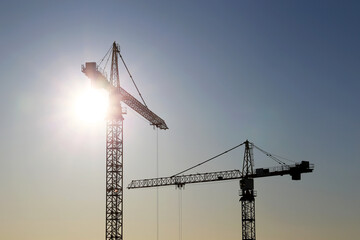 Silhouettes of two construction cranes against sunshine. Housing construction