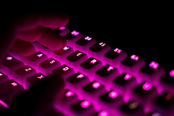 side view of fingers typing on illuminated RGB keyboard in the dark