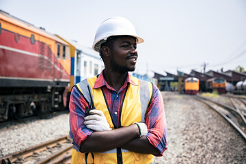 Portrait of Africa American engineering using walkie talkie with wear hardhat in front of train garage. Back view of contractor on background of outdoor modern steel factory.