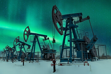 Oil pump - Nodding donkey. Night view. Oil industry equipment. Oil field pump jack and oil refinery in the winter with snow, mountains and forest in background.