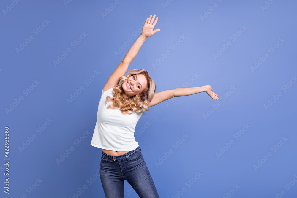 Wall mural Portrait of charming cheerful wavy-haired girl dancing having fun stretching isolated over blue color background