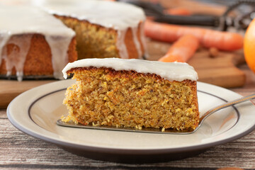 Piece of fresh baked carrot cake with lemon glaze on a plate with cake server