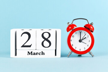 Concept for time change for daylight saving summer time in Europe on March 28th with red alarm clock and calendar on blue background