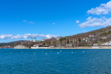 Fototapeta premium Panoramic view of Lake Abrau Dyurso in Krasnodar Krai, Russia. Picturesque view of blue lake with church on sunny spring day in Abrau Durso.