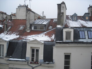 Toits de Paris en tuiles et zinc, partiellement enneigés, avec cheminées, combles, fenêtres et lucarnes