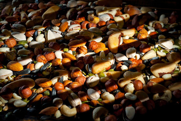 Many types of nuts close up. Textures of different nuts. Nuts are dumped in a pile. Contrasting dramatic light as an artistic effect.