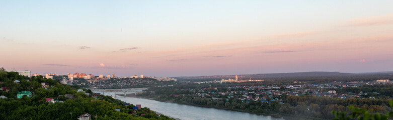 Panoramic photo of Ufa skyline in city center with buildings, river, forest area on beautiful pink-blue sunset. Observation deck on city. Impression of traveler. Poster or postcard with view of city.