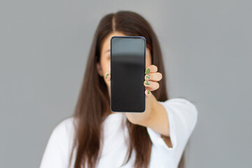 Close up portrait of a smiling woman showing blank screen mobile phone while standing isolated over gray background
