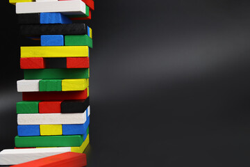 Fototapeta na wymiar Game tower of colored wooden blocks, bricks on a black background. Copy space for text