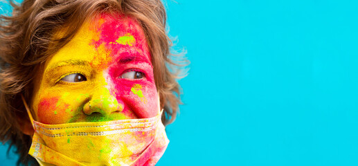 Portrait of a woman in dry color holi paint and medical protective mask. Holi celebration during a pandemic. Close-up face in bright colors, copy space