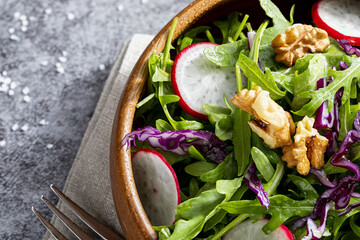 Appetizing and healthy low calorie salad with arugula, radishes, red cabbage and walnuts. In a wooden bowl and homemade look. Mediterranean diet. With Copy space.