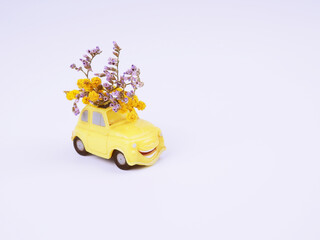 Small yellow toy car with a bouquet of wild flowers on a white background