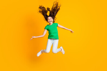 Full size photo of happy excited funky funny little girl jumping with flying hair isolated on yellow color background