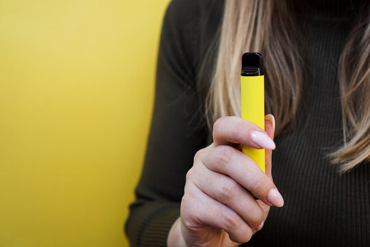 Yellow disposable electronic cigarette in female hand. Bright yellow background