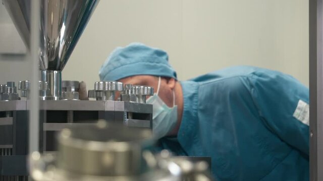 Medicine Factory. A worker is wearing the uniform and a mask is configuring the Medical encapsulation machine to get the most precise setting. Pill Supply Production. Automatic Equipment.