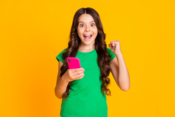 Photo of happy excited smiling cheerful crazy girl raise fist in victory success use cellphone isolated on yellow color background