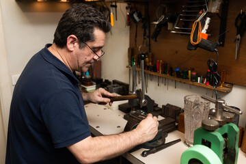 jeweler goldsmith picks a piece of square with a hammer on an anvil