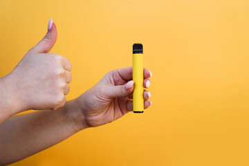 Yellow disposable electronic cigarette in female hand. Hand shows thumbs up