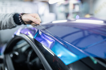 Car wrapping specialist putting vinyl foil or film on car. Selective focus.