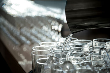 pouring cool pure transparent clear drinking water from the jar to clean glasses on the table