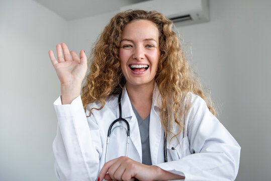Happy smiling young female doctor waving hand greeting patient online via video call, home medical consulation service concepts