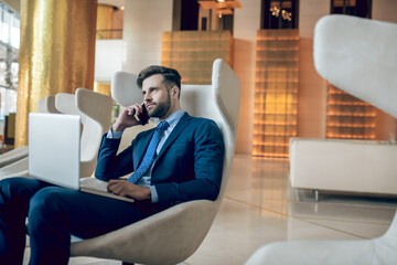 Obraz premium Man in a suit sitting in the arm-chair and working on a laptop