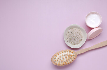 Top view of bowl of skin renewing scrub, lotion and dry wooden brush on the pink surface.Empty space