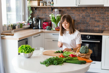Brunette Woman in white t-shirt preparing vegetable salad in the kitchen at home, Wife Cutting ingredients on table. Healthy Food, Vegan Salad. Dieting Concept.