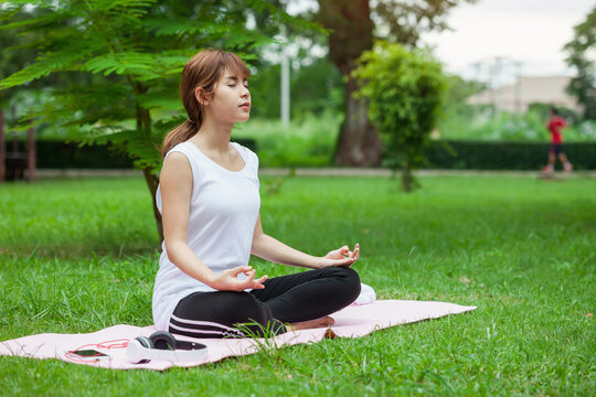 Image of Asian woman sitting and meditation yoga lotus pose outdoor park.
