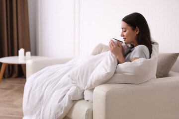 Woman covered in blanket holding cup of drink on sofa, space for text