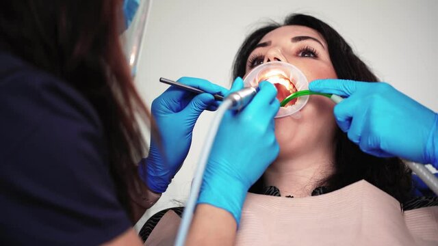 Close-up process of brushing teeth in dental clinic. A professional dentist treats teeth with a special instrument for female patient. Working process in dentistry. Healthcare and medicine concept.