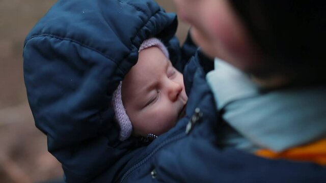 Portrait of a toddler in a sling jacket in the fall. Walk with the child in the park. Natural parenting. The hood is worn on the head.