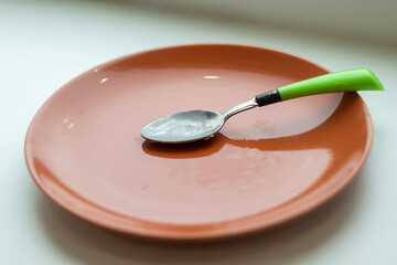empty dirty orange plate with a spoon on the table close up